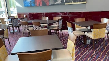 A restaurant with a modern interior, featuring a mix of wooden and upholstered chairs, a patterned carpet, and a large abstract painting on the wall.