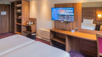 A hotel room with a large bed, wooden shelving, a flat-screen TV mounted on the wall, and a desk with a chair.