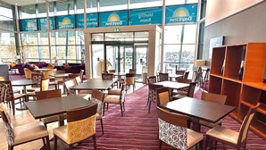 A hotel lobby with multiple seating areas, including tables and chairs, and a large window providing a view of the city. - Days Inn by Wyndham Wetherby (Wetherby)