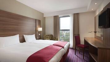 A hotel room with two beds, a desk, a TV, and a view of the outdoors.