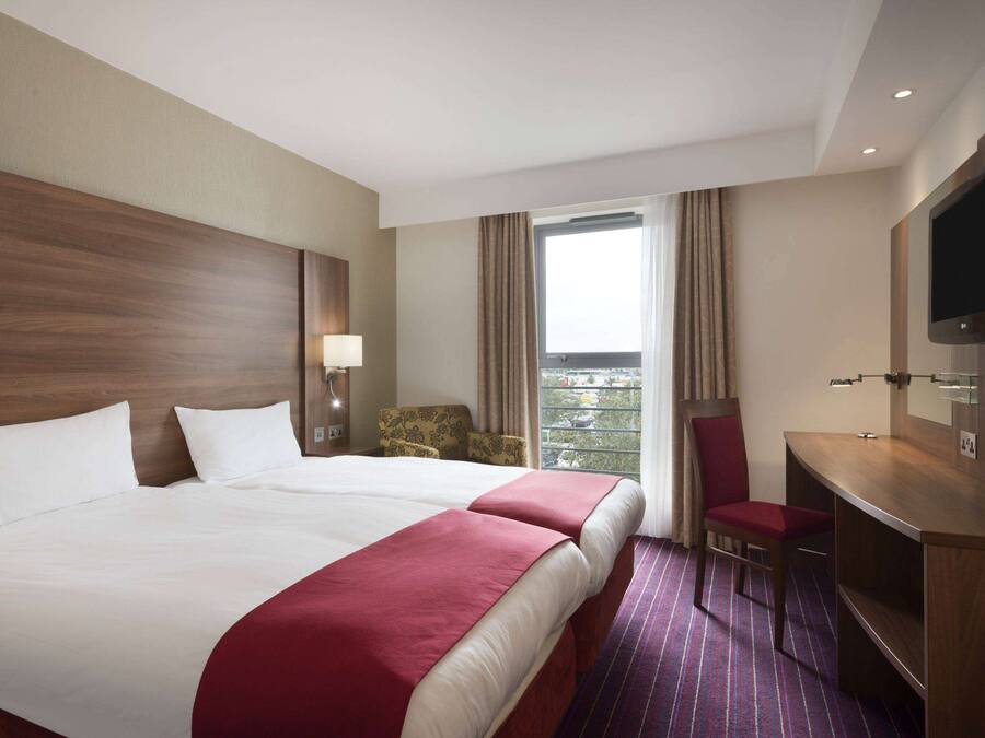 A hotel room with two beds, a desk, a TV, and a view of the outdoors.