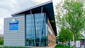 A Days Inn hotel with a modern glass facade, a signboard advertising hotel and meeting room services, and a parking area with electric vehicle charging stations. - Days Inn by Wyndham Wetherby (Wetherby)