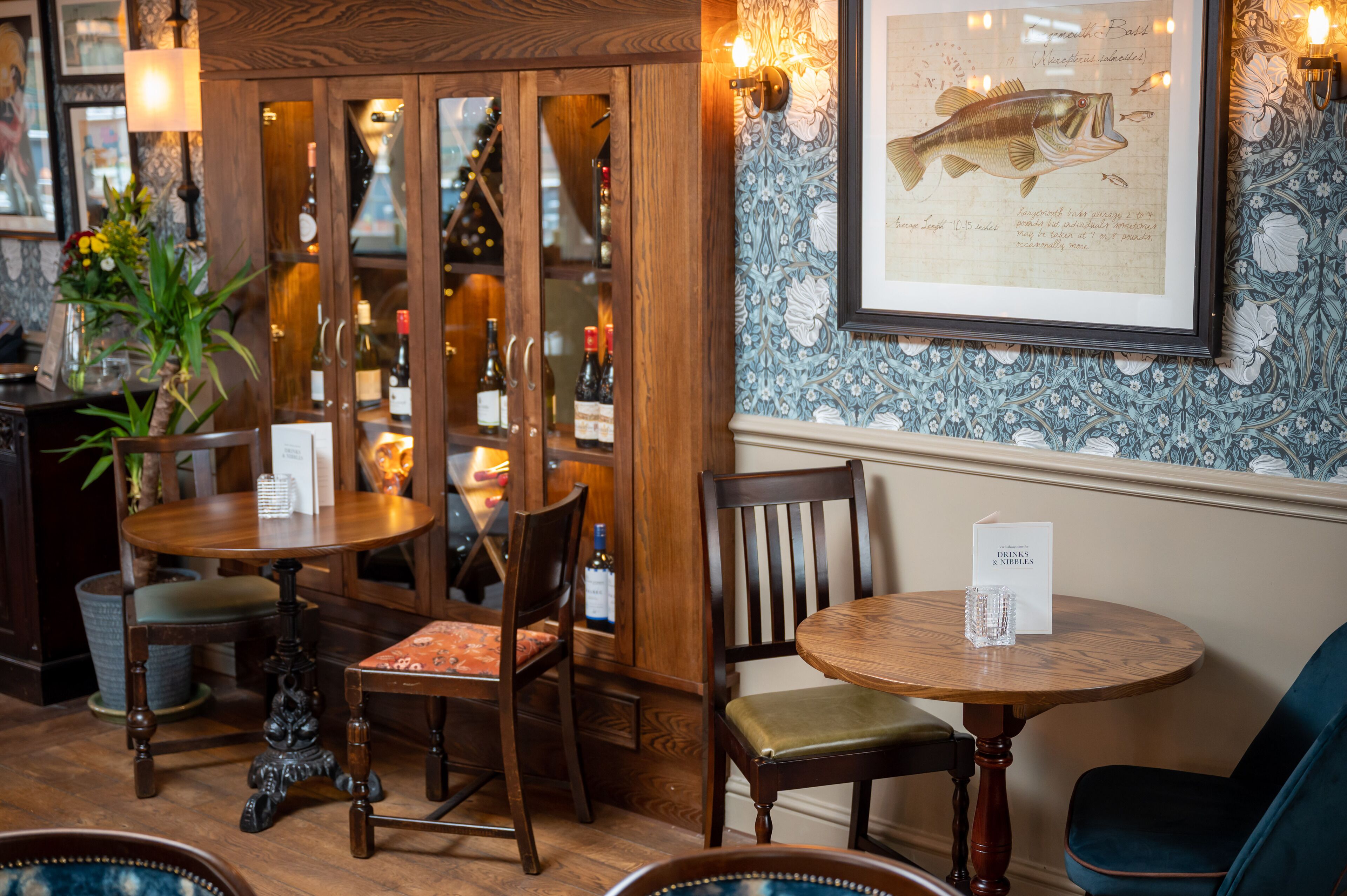 A restaurant interior with wooden tables and chairs, a menu stand, and a framed fish illustration on the wall.