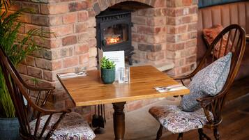 A wooden table with two chairs, a brick fireplace, and a potted plant.