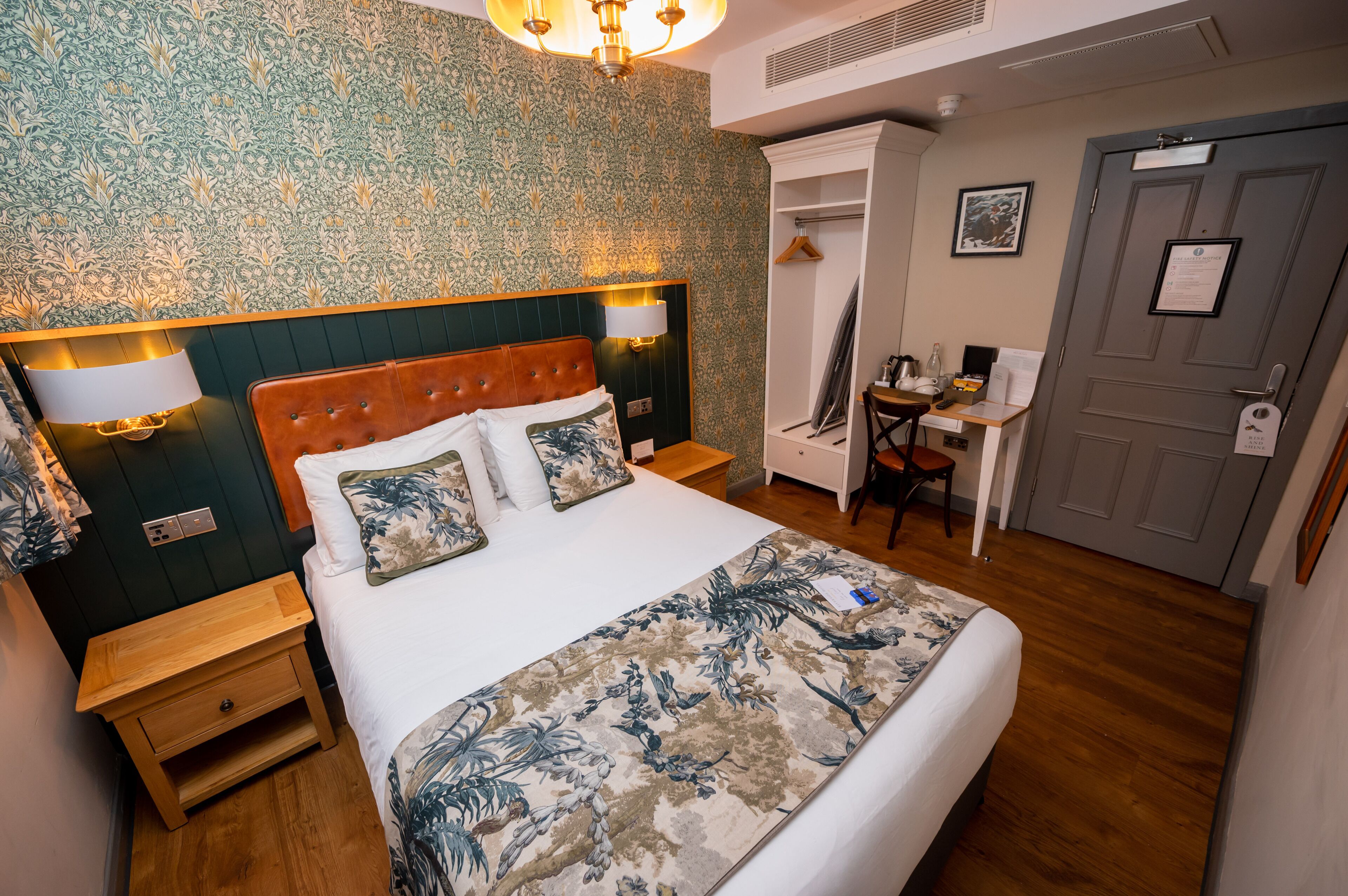 A hotel room with a large bed, a desk, and a wardrobe.