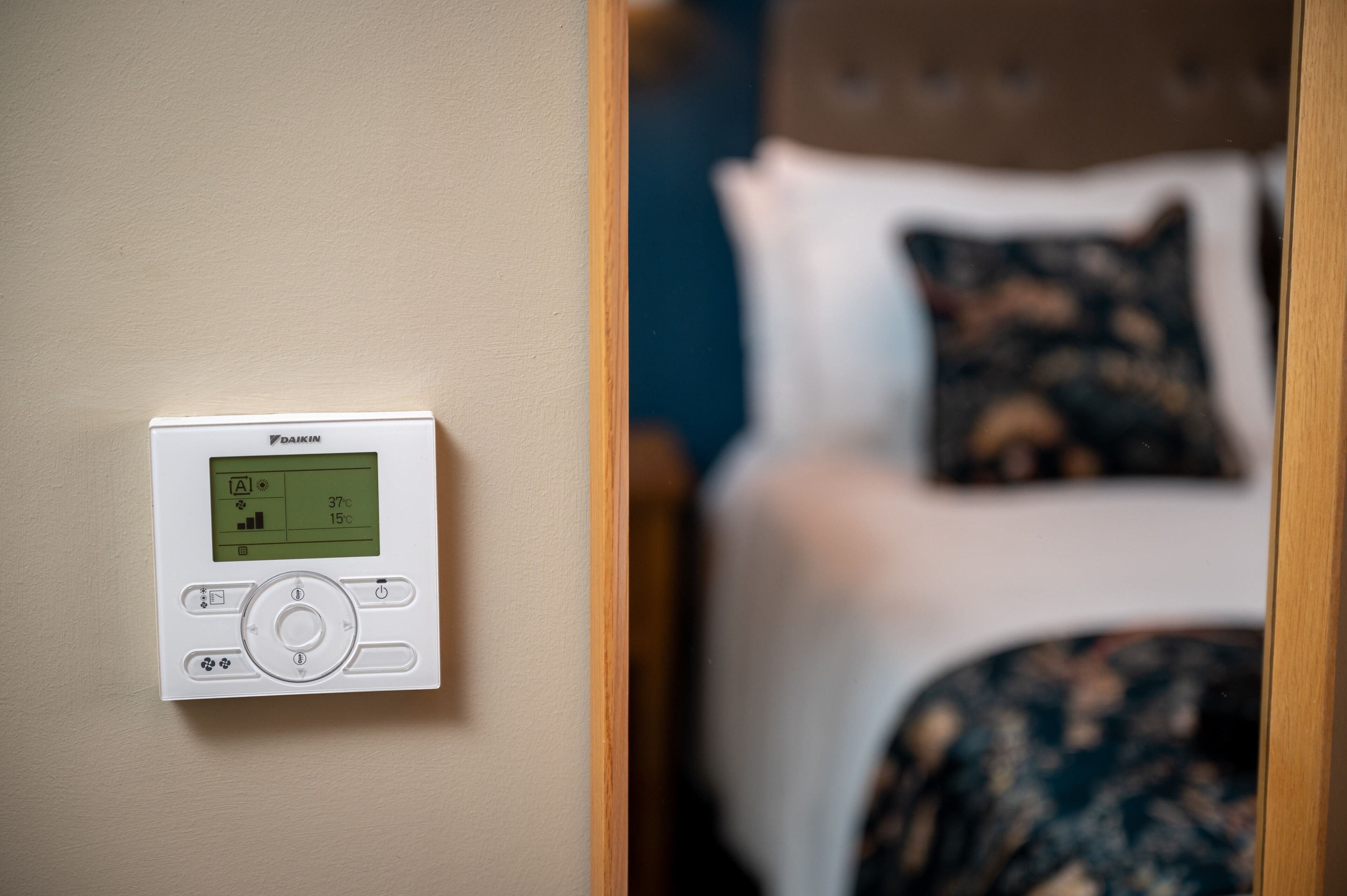 Ein Thermostat an der Wand, im Hintergrund ein Bett.