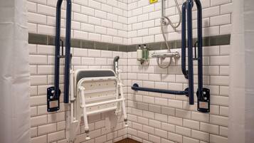 A corner of a bathroom with white tiled walls, a shower area, and a wheelchair-accessible bench.