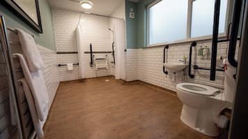 A bathroom with a wooden floor, white tiled walls, a white toilet, a sink, and a shower area.