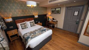 A bedroom with a large bed, wooden nightstands, a desk, and a door.