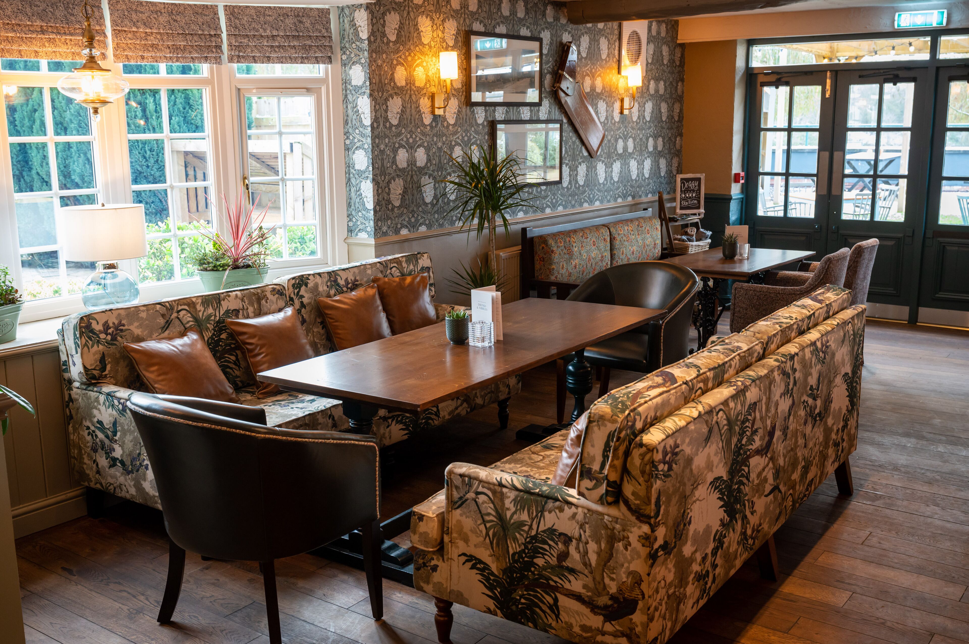 A cozy dining area with a wooden table, cushioned seating, and a view of the outdoors through large windows.
