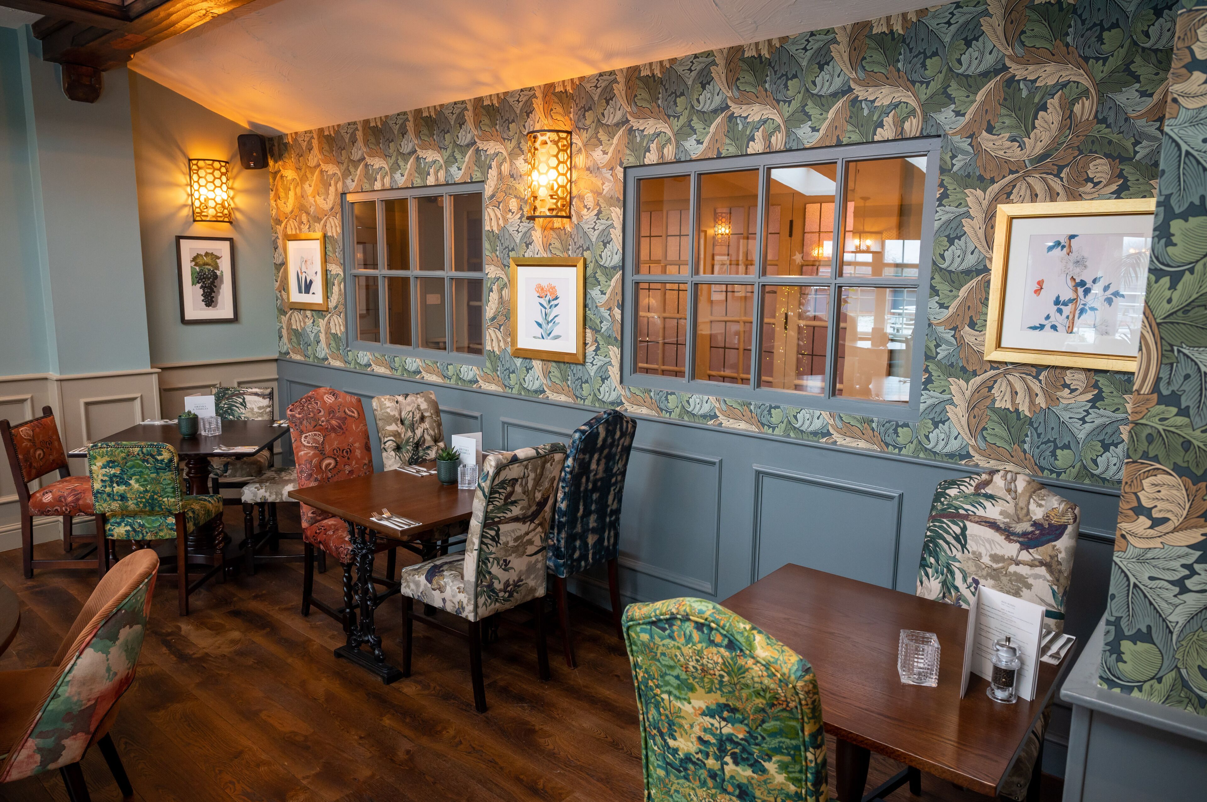 A dining area with patterned wallpaper, wooden tables, and upholstered chairs.