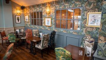 A dining area with patterned wallpaper, wooden tables, and upholstered chairs.
