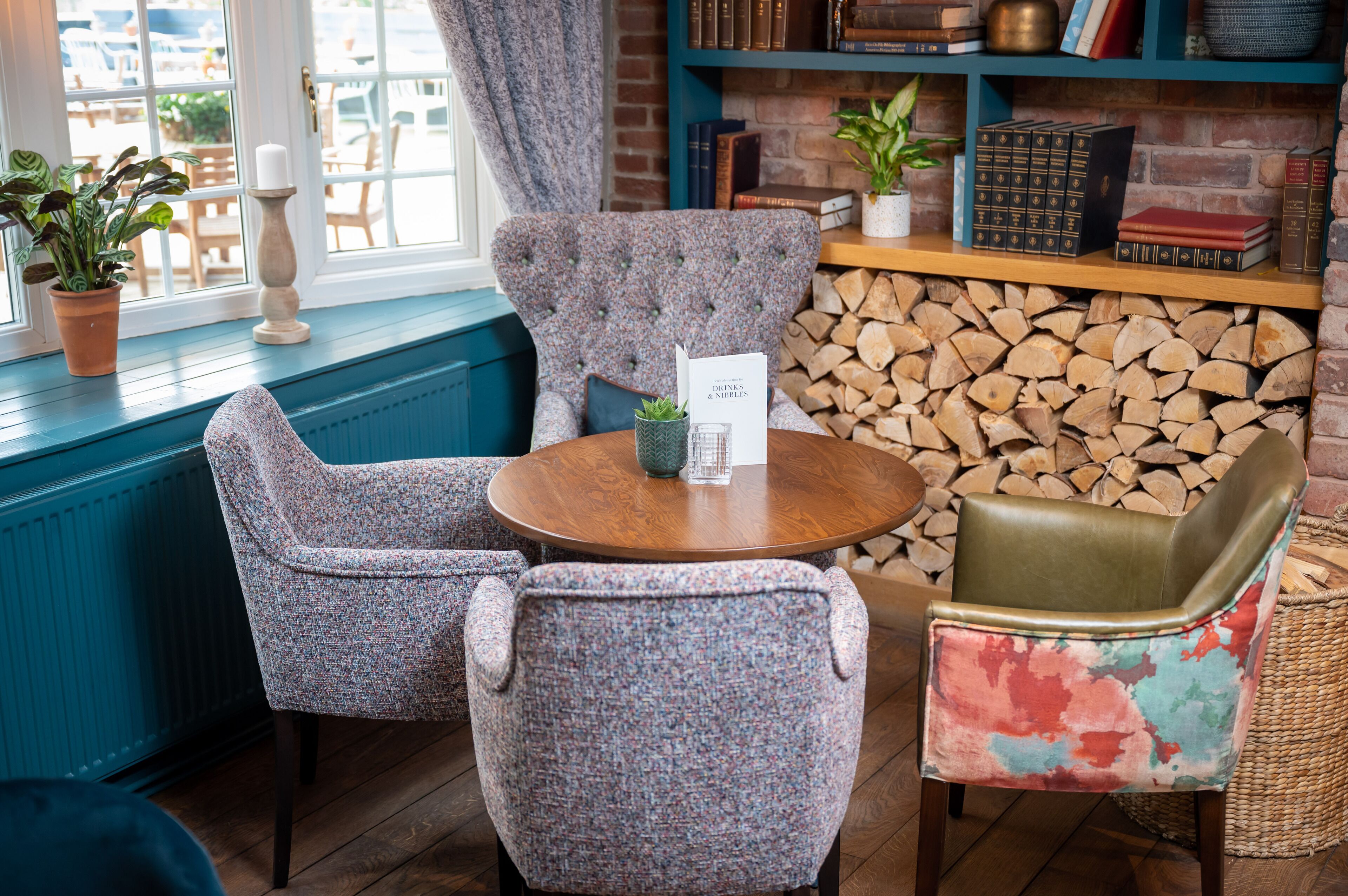 Un coin salon accueillant avec une table ronde en bois, deux fauteuils à motifs et un fauteuil aux couleurs vives. Un menu est posé sur la table.