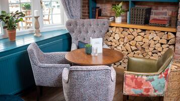 Un coin salon accueillant avec une table ronde en bois, deux fauteuils à motifs et un fauteuil aux couleurs vives. Un menu est posé sur la table.
