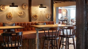 A cozy restaurant interior with a wooden bench seating area, wooden tables, and rustic decor. - Swan Hotel Thaxted by Greene King Inns (Dunmow)