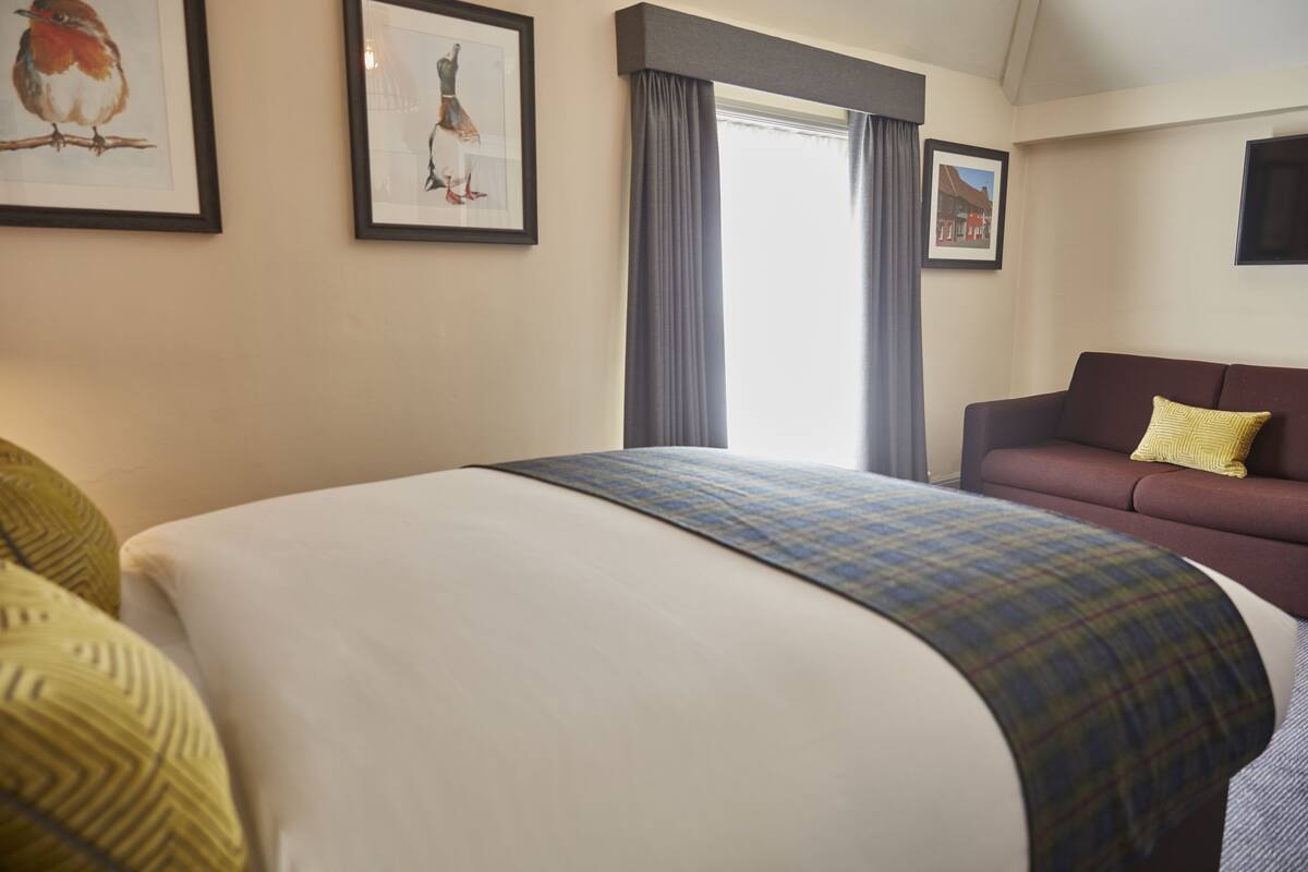 A hotel room with a large bed, a sofa, and two framed pictures on the wall.