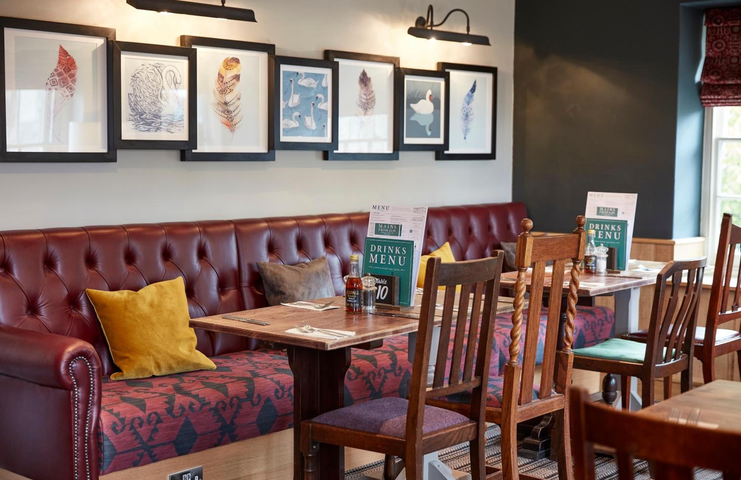 A restaurant with a red leather booth, wooden chairs, and framed artwork on the wall.