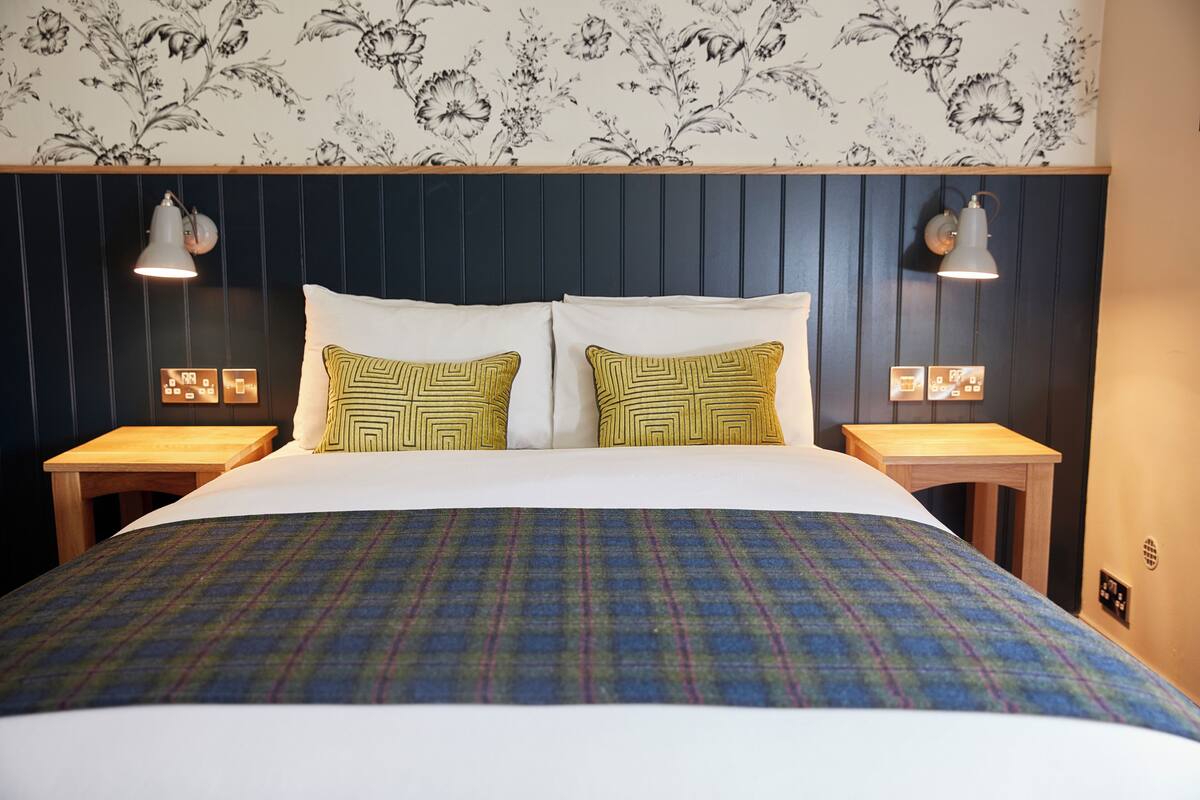 A neatly made bed with a plaid bedspread, two pillows with geometric patterns, and two bedside tables with lamps.