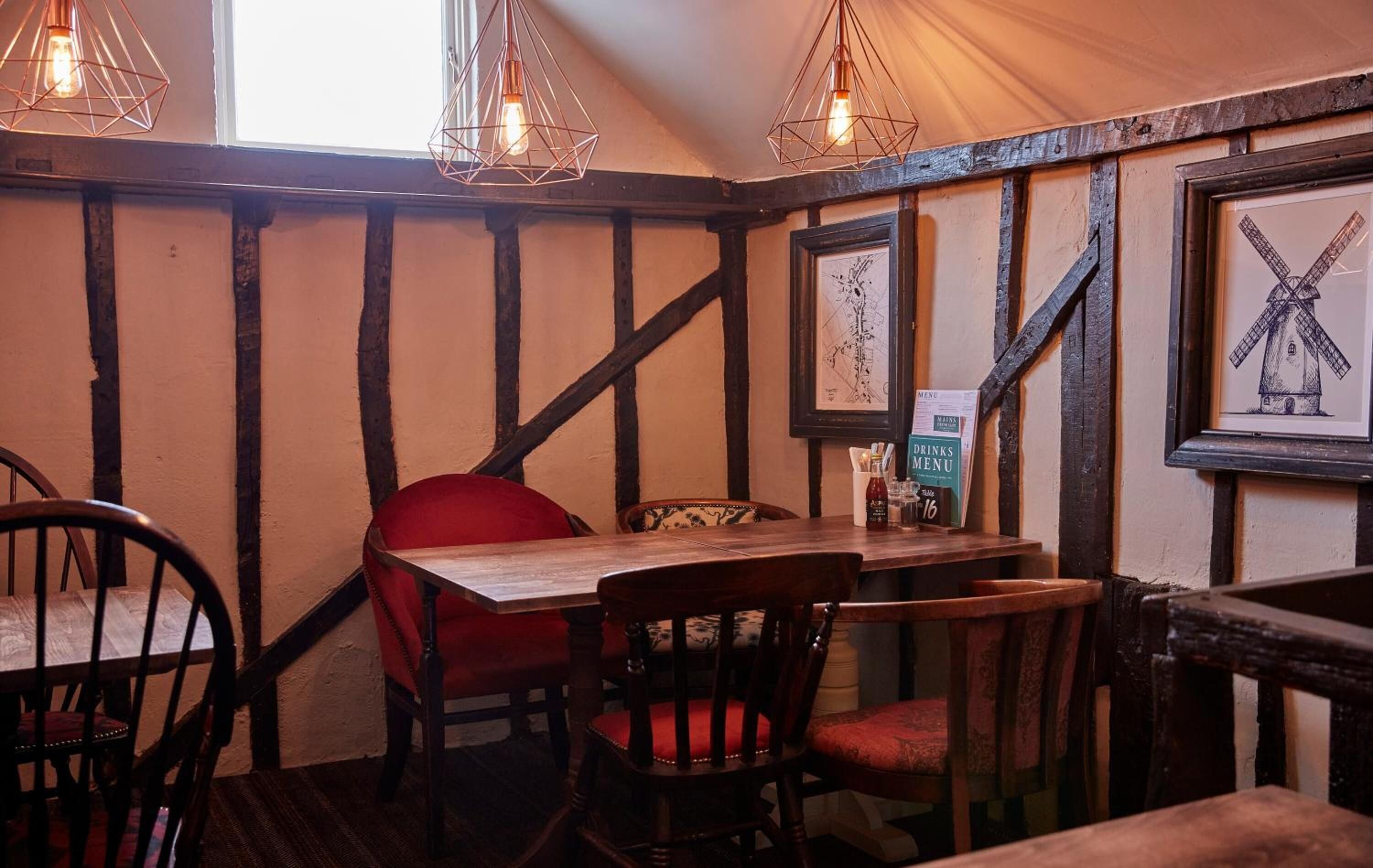 A rustic interior with exposed wooden beams, a wooden table with chairs, and a menu board.