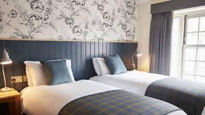 A hotel room with two beds, a wooden headboard, floral wallpaper, and a window with curtains. - Swan Hotel Thaxted by Greene King Inns (Dunmow)