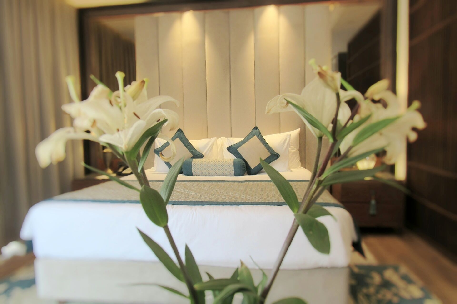 A neatly made bed with white linens and blue pillows, surrounded by white flowers.