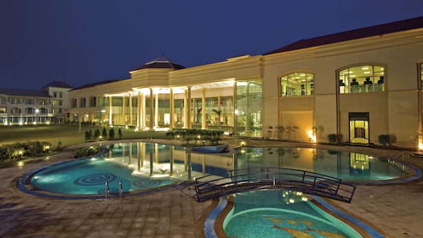 Un hotel con una amplia piscina al aire libre, un área techada con asientos y una fachada de edificio bien iluminada.