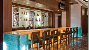 Zona de bar con una barra larga, varios taburetes y un elemento decorativo de iluminación.