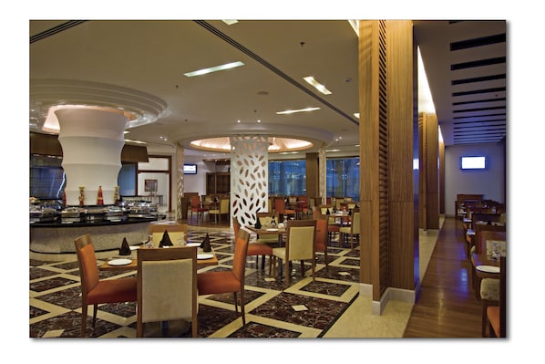 A spacious hotel lobby with a central bar area, multiple seating arrangements, and a patterned floor.