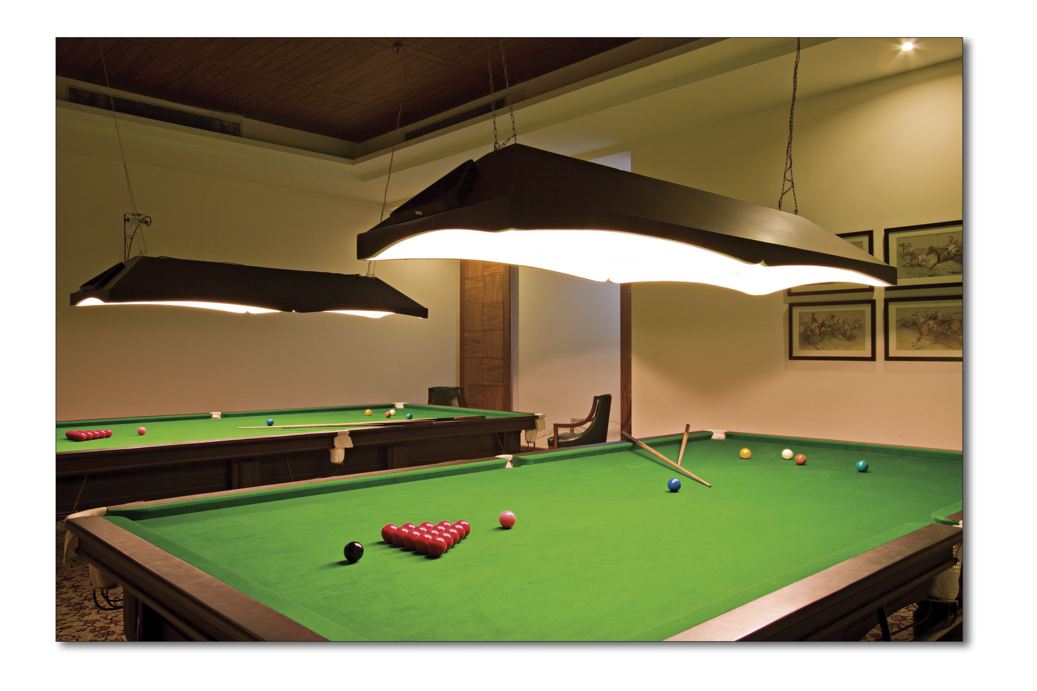 A pool table with balls, overhead lighting, and framed artwork on the wall.
