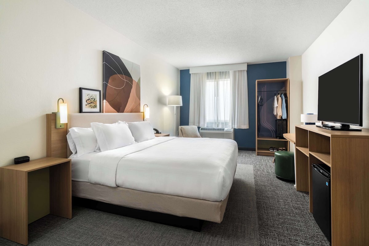 A hotel room with a large bed, bedside tables, a TV, a wardrobe, and a window with curtains.