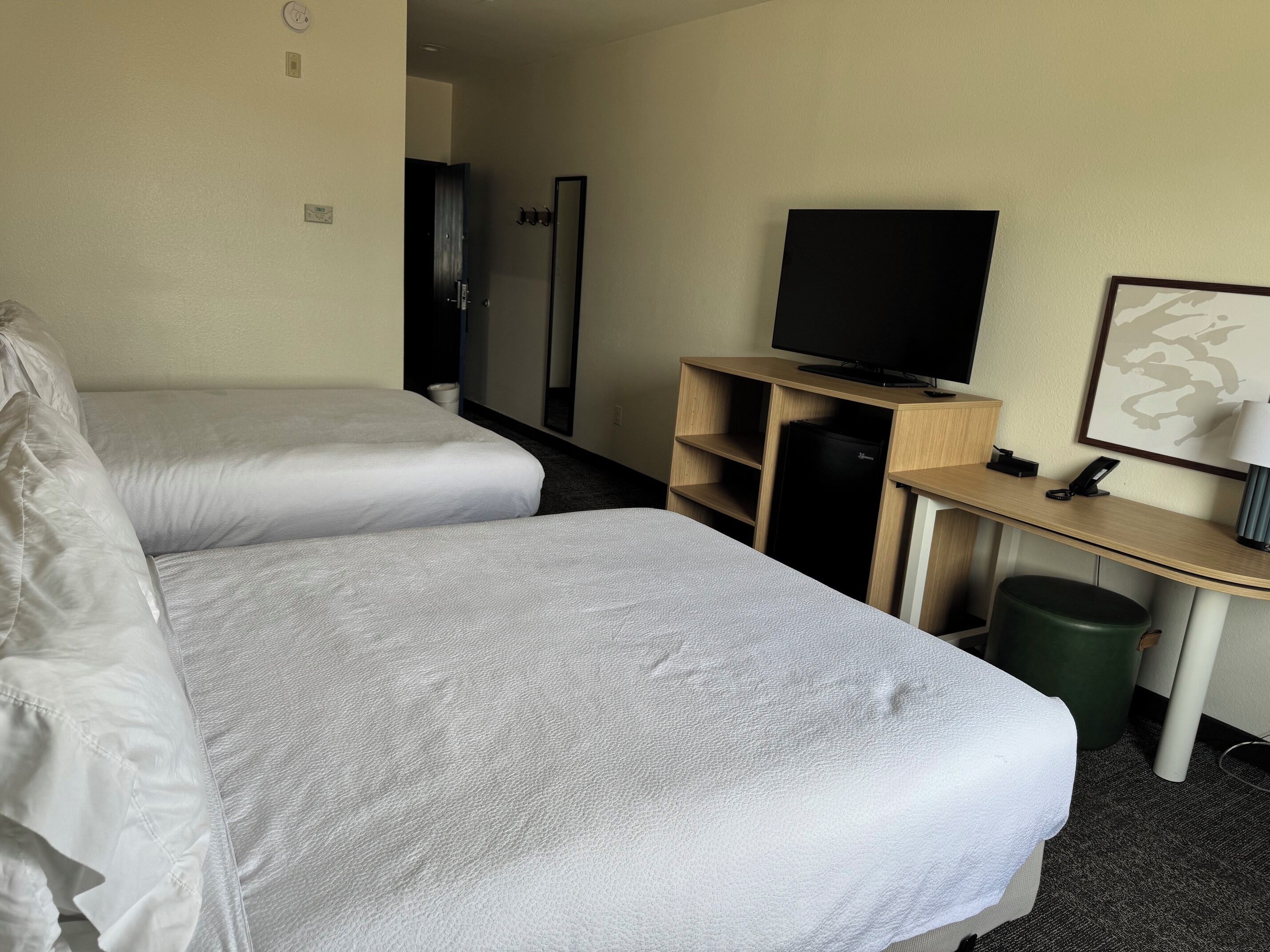 A hotel room with two beds, a TV, a desk with a lamp, and a trash can.