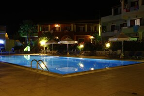 A swimming pool with lounge chairs and umbrellas, surrounded by buildings with balconies and lights.