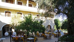 Un espace extérieur aménagé en terrasse, avec des tables et des chaises jaunes, entouré d’arbres et bordé d’un bâtiment doté de nombreuses fenêtres et de balcons.