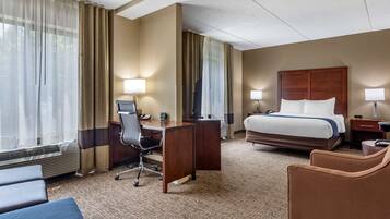 Una habitación de hotel con cama, escritorio, silla y un amplio ventanal con cortinas.