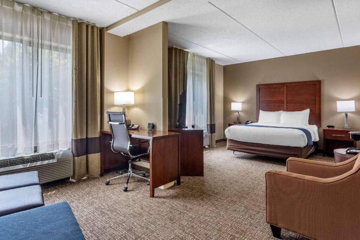 A hotel room with a bed, desk, chair, and a view of the outdoors.