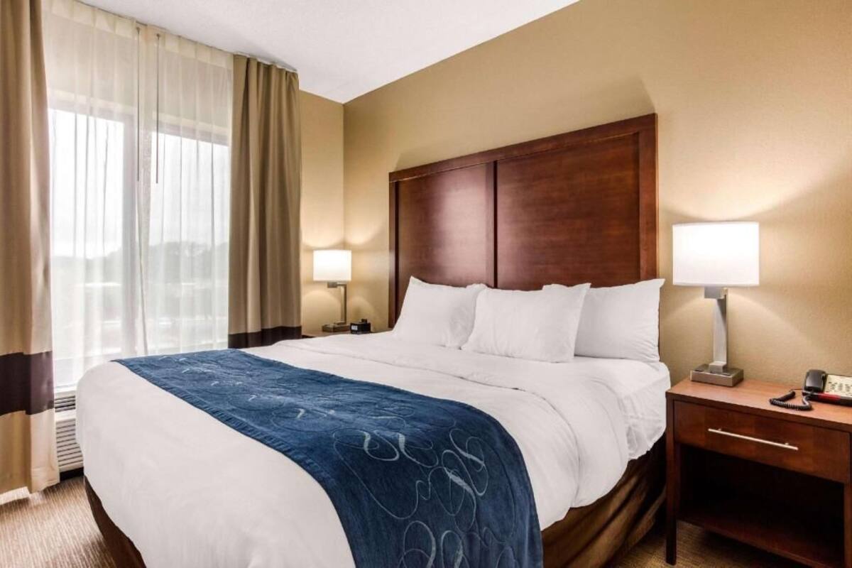 A hotel room with a large bed, two bedside tables with lamps, a wooden headboard, and a window with curtains.