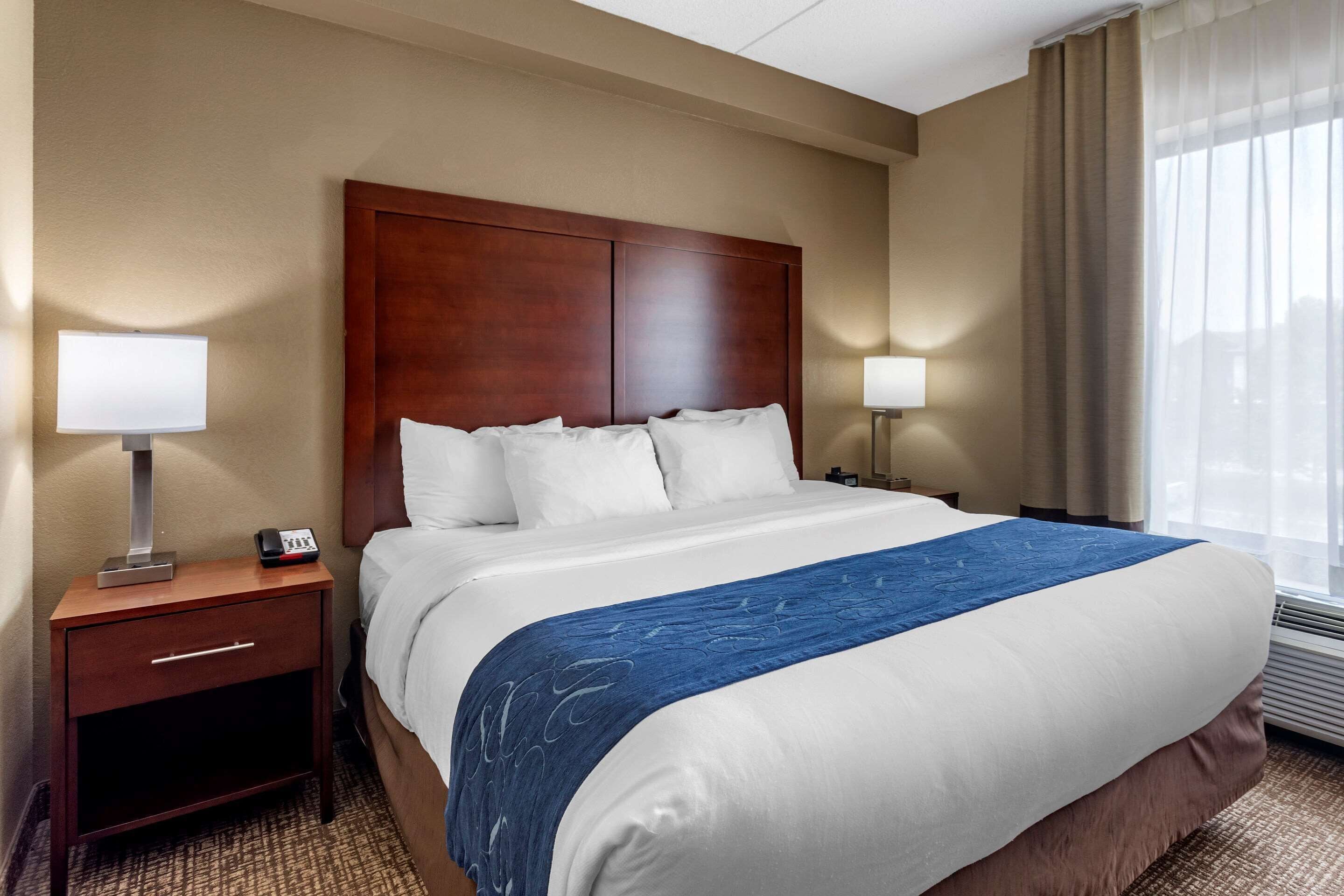 A hotel room with a large bed, two bedside tables, a nightstand, a lamp, and a window with curtains.