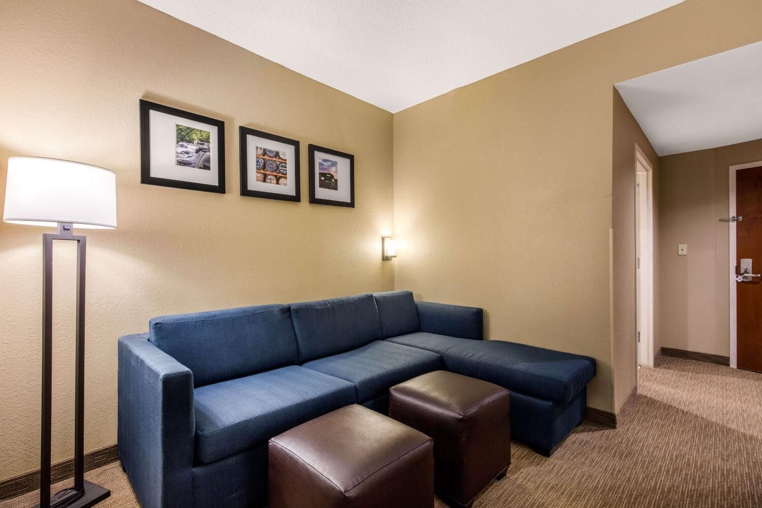 Habitación de hotel con sofá modular, lámpara de pie y tres cuadros en la pared.