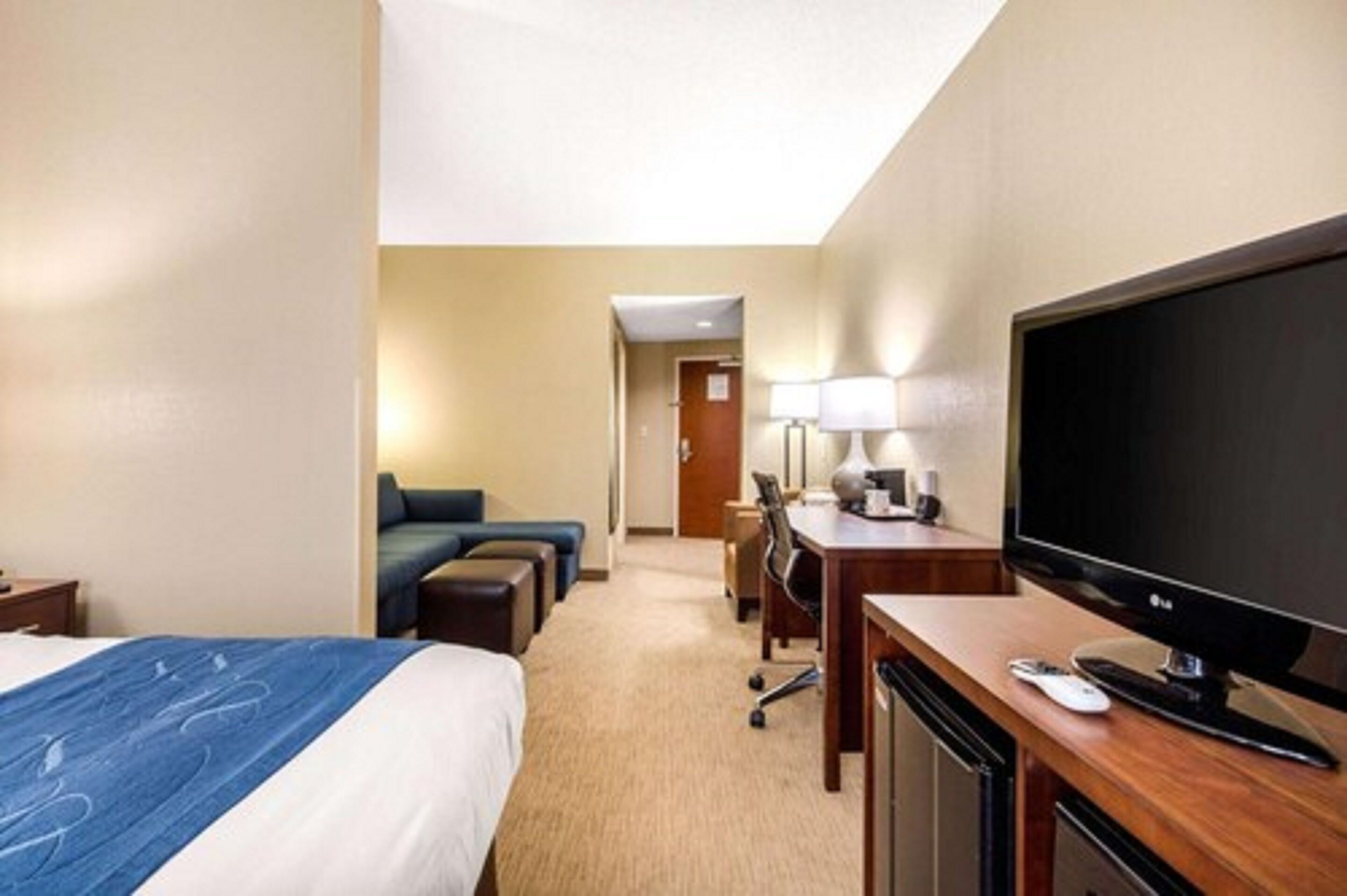 A hotel room with a bed, a desk with a TV, a chair, and a lamp.
