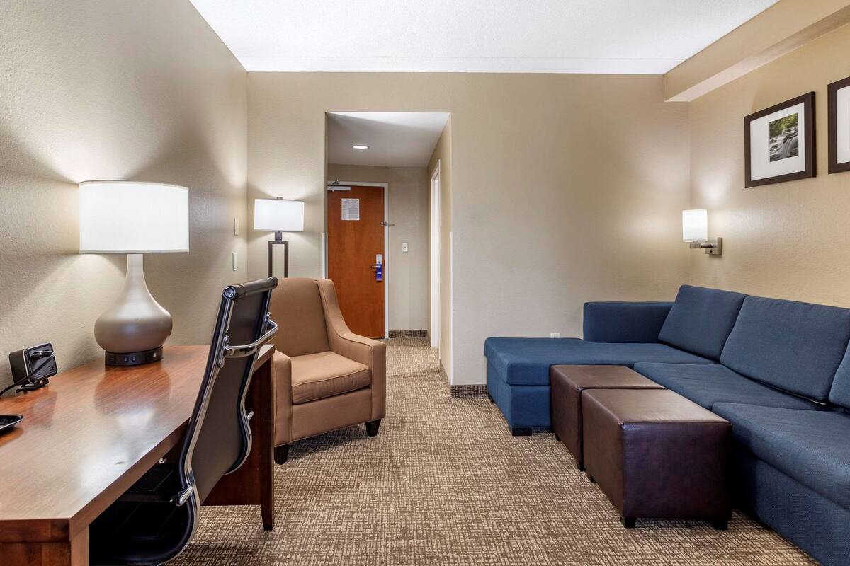 A hotel room with a desk, chair, sofa, and ottoman.