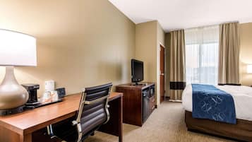 Ein Hotelzimmer mit Schreibtisch, Stuhl, Fernseher, Minibar und einem Bett mit blauer Decke.