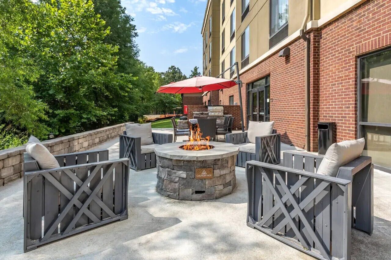 An outdoor patio with a stone fire pit, seating, and a red umbrella.
