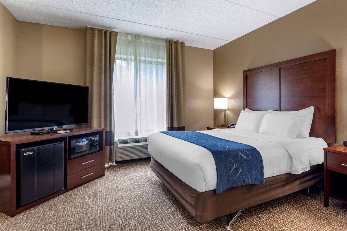 A hotel room with a bed, a TV, a desk, and a lamp.