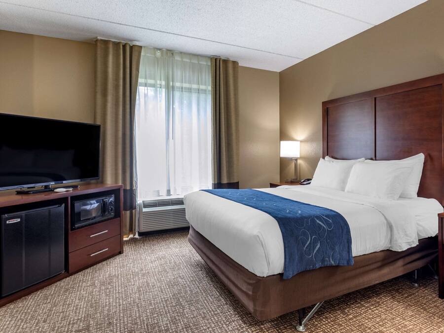 A hotel room with a bed, a TV, a desk, and a lamp.