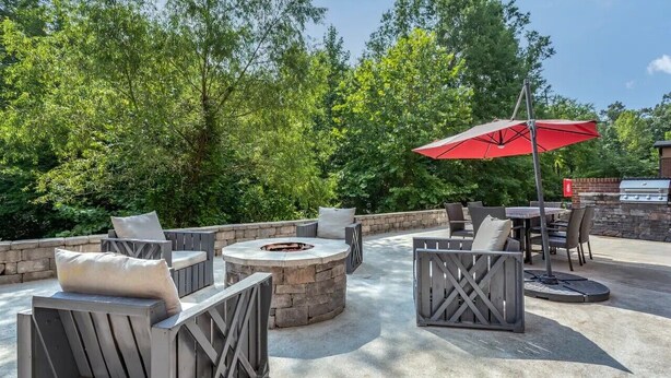 Une terrasse extérieure avec des sièges en pierre, un foyer et un parasol rouge.