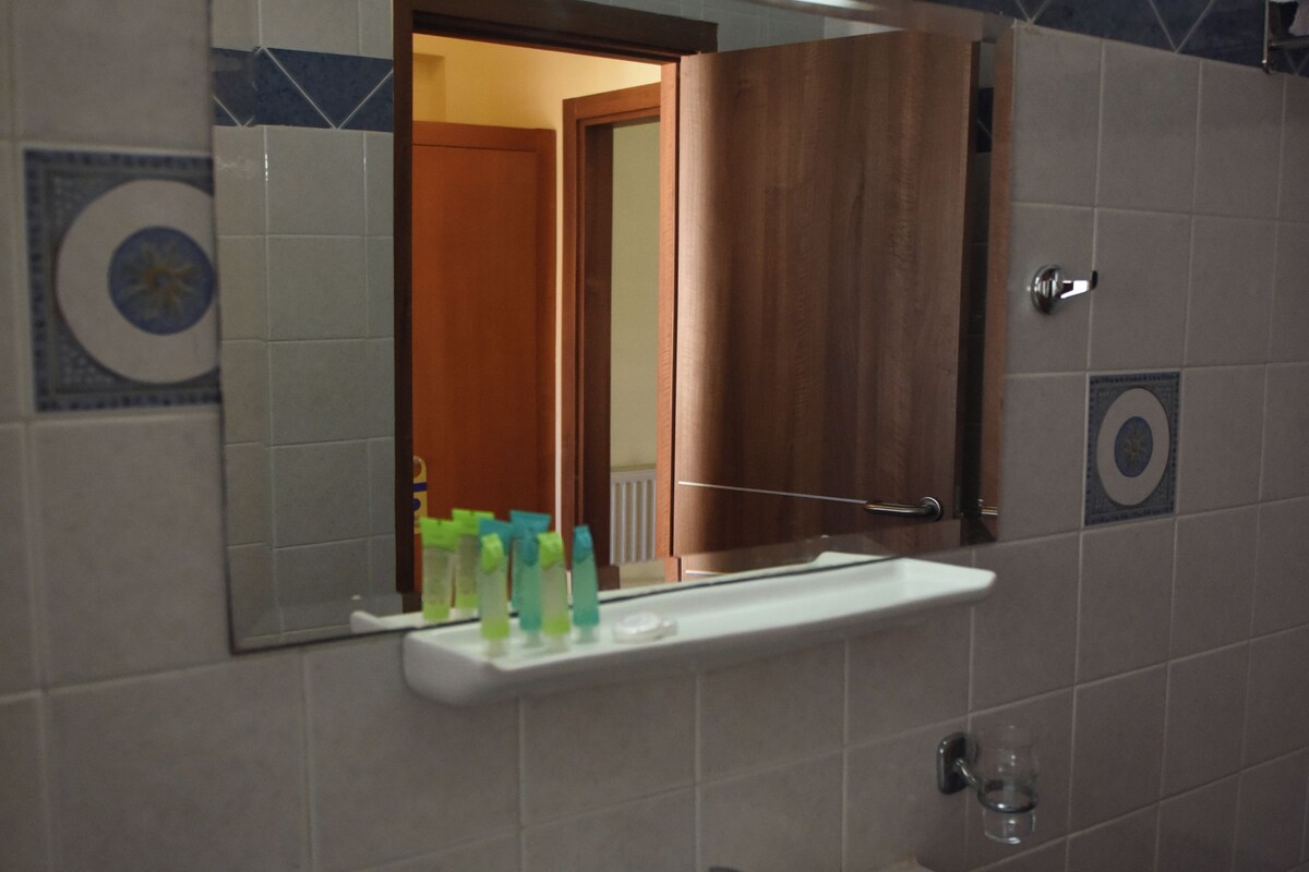 Une salle de bain équipée d’un lavabo, d’un miroir et d’une étagère où sont rangés les articles de toilette.