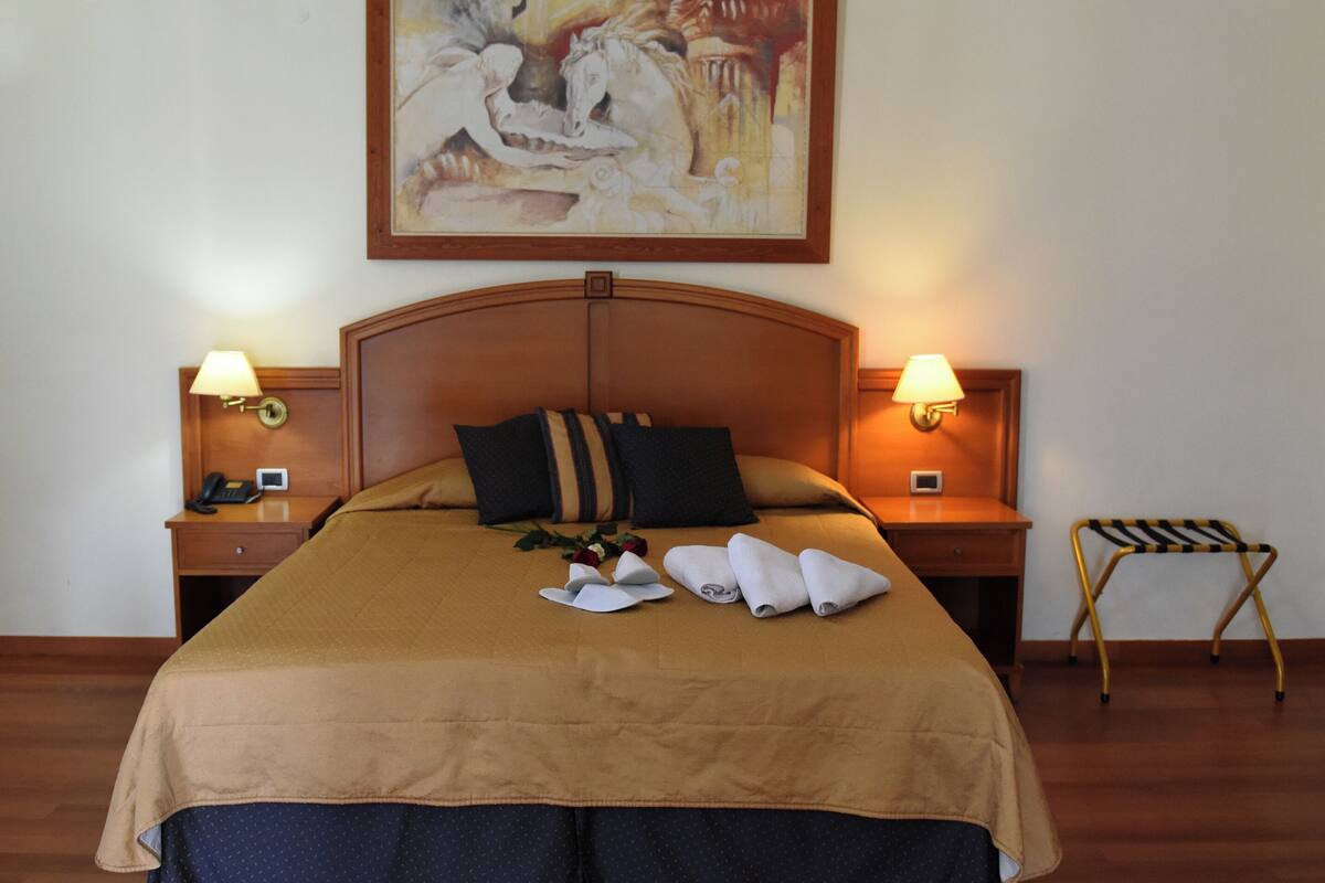 Une chambre d’hôtel avec un grand lit, deux tables de chevet avec des lampes, une tête de lit en bois et un tableau au-dessus du lit.