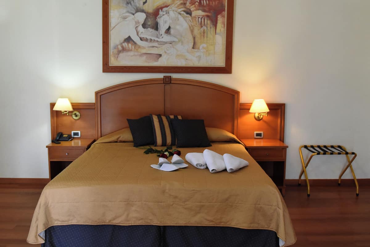 A hotel room with a large bed, two bedside tables with lamps, a wooden headboard, and a painting above the bed.