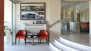 A modern hotel lobby with a curved staircase, a reception desk, and red chairs. - Blue Sea (Lesvos)