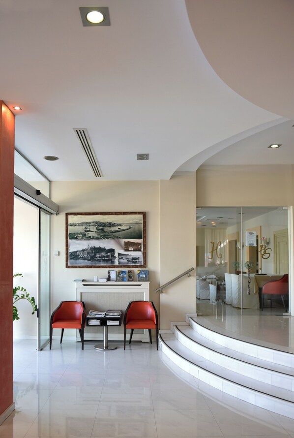 A modern hotel lobby with a curved staircase, a reception desk, and red chairs.
